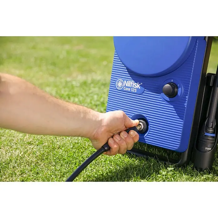 Nilfisk Hidrolimpiadora de alta presión CORE 125 Home - 125 bar, 1.400 W, Capacidad de bombeo: 438 l/h - Primer plano de una hidrolimpiadora Nilfisk Core 125 con una mano conectando una manguera.