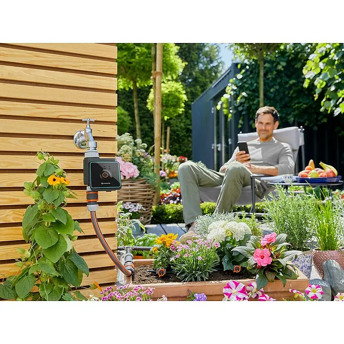 Gardena Bewässerungscomputer Bluetooth - Bewässerungsdauer: 1 min - 480 min - Gardena Bewässerungssteuerung am Wasserhahn mit Mann im Hintergrund. Ermöglicht bequeme und präzise Gartenbewässerung.