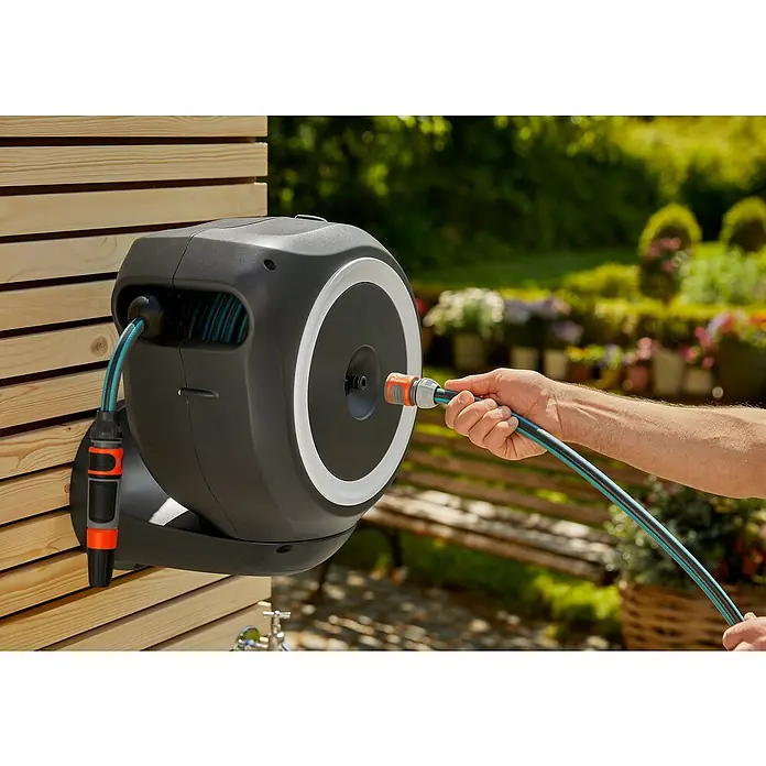 Gardena Wand-Schlauchbox RollUp M - Schlauchlänge: 20 m - Eine Gardena Schlauchtrommel an einer Holzwand mit einem angeschlossenen Schlauch, der von einer Hand gehalten wird.