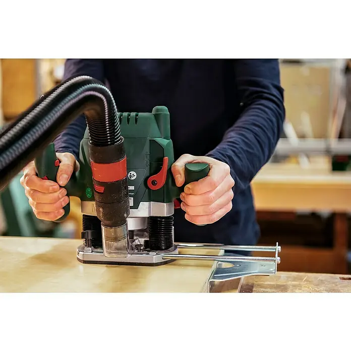 Bosch Oberfräse POF 1200 AE - 1.200 W, 55 mm - Eine Person, die eine Oberfräse mit Staubsaugeranschluss verwendet, um präzise Schnitte in ein Holzstück zu machen.