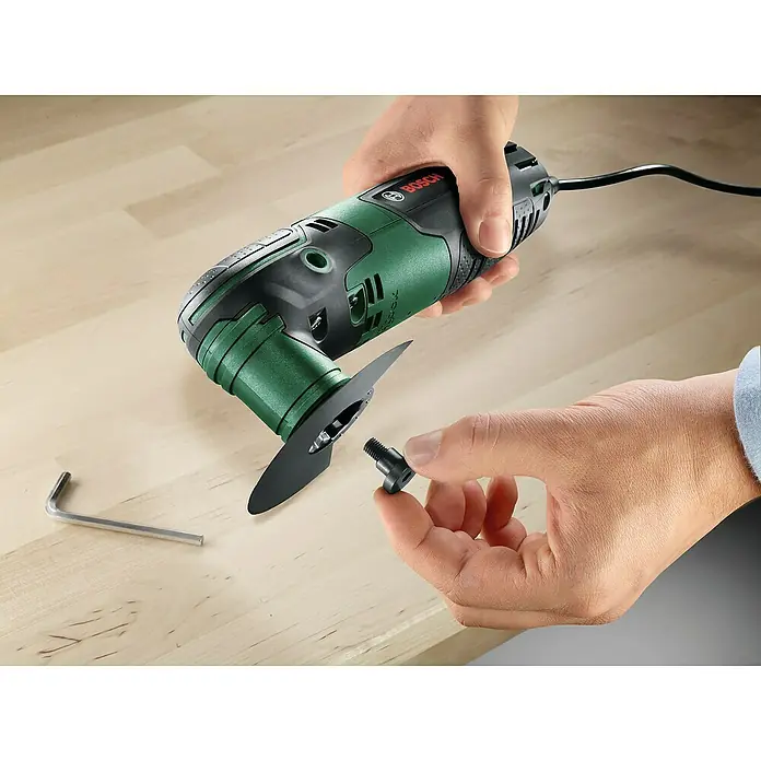 Bosch Elektro-Multifunktionswerkzeug PMF 220 CE - 220 W, STARLOCK-System - Nahaufnahme eines grünen Bosch Multifunktionswerkzeugs mit Zubehör auf einem Holztisch, das die Vielseitigkeit des Produkts hervorhebt.