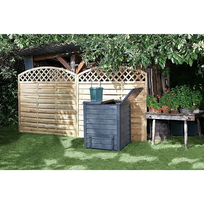 Garantia Komposter Thermo-Wood - 400 l, 72 x 72 x 90 cm, Mit Bodengitter - Gartenszene mit einem stilvollen, grauen Komposter aus Holz neben einem Holzzaun und unter üppigem Grün.