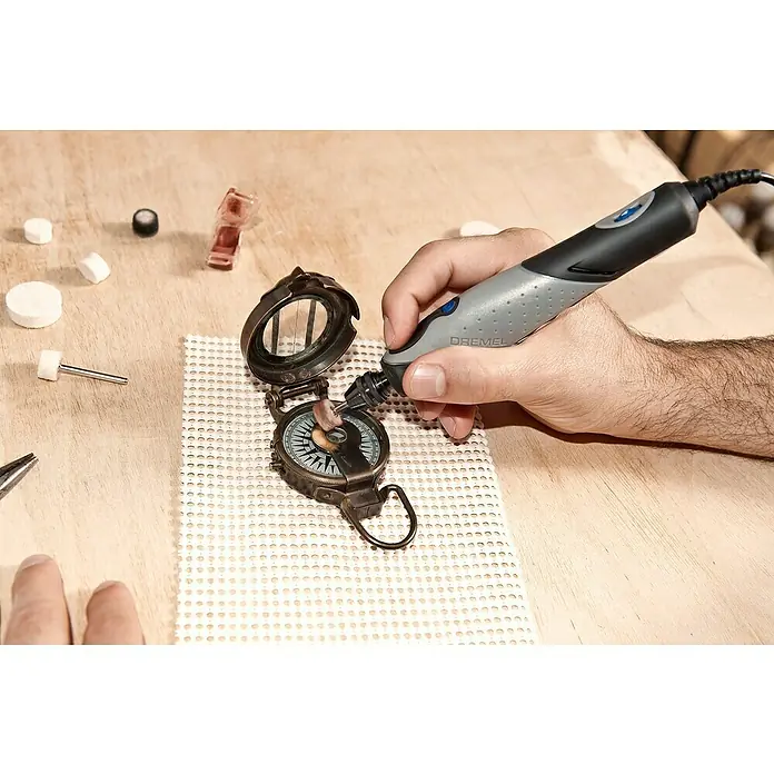 Dremel Elektro-Multifunktionswerkzeug 2050 Stylo+ - 9 W - Detaillierte Nahaufnahme eines Dremel-Werkzeugs beim Polieren eines antiken Kompasses, mit Polierzubehör auf einer Holzoberfläche.