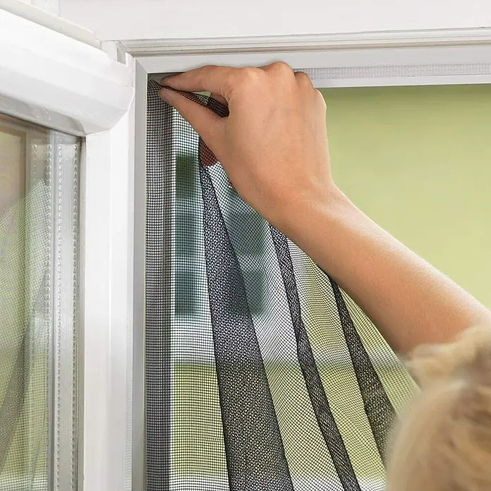 Tesa Insect Stop Cinta para mosquitera Comfort - Largo: 5,6 m, Blanco - Persona que fija una mosquitera magnética negra a un marco de ventana blanco. Este producto protege de los insectos.