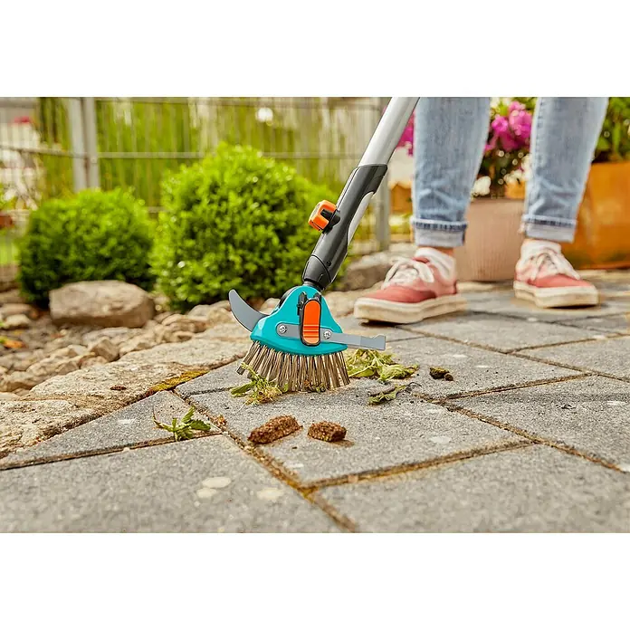 Gardena Combisystem Fugenkratzer 3in1 - Länge: 23,5 cm, Material Gerätekopf: Edelstahl - Eine Person benutzt eine Gardena Fugenkratzer-Bürste, um Unkraut und Schmutz von Pflastersteinen im Garten zu entfernen.