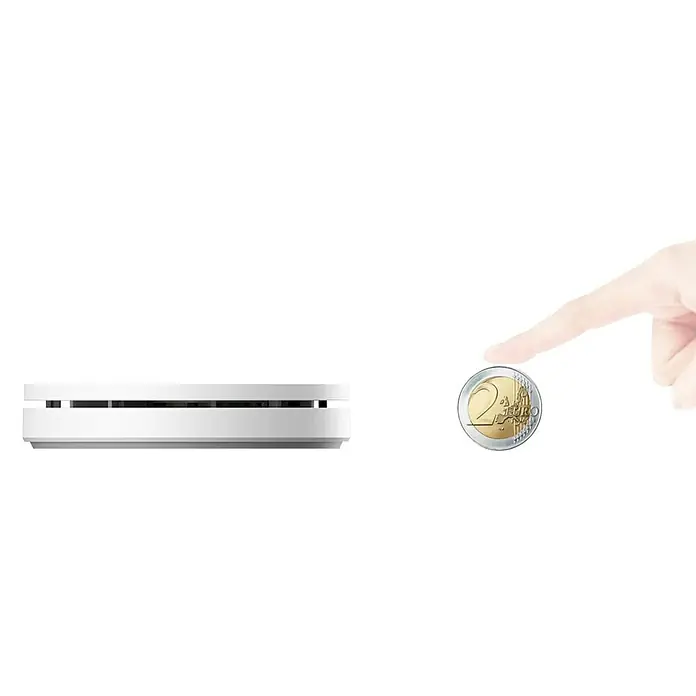 UniTEC Rauchwarnmelder Design - Durchmesser: 12,5 cm, Höhe: 2,5 mm, Alarmsignal: 85 dB, Weiß - Eine Nahaufnahme eines schlanken, weißen Heizkörperthermostats neben einer Zwei-Euro-Münze und einer Hand zur Größenansicht.