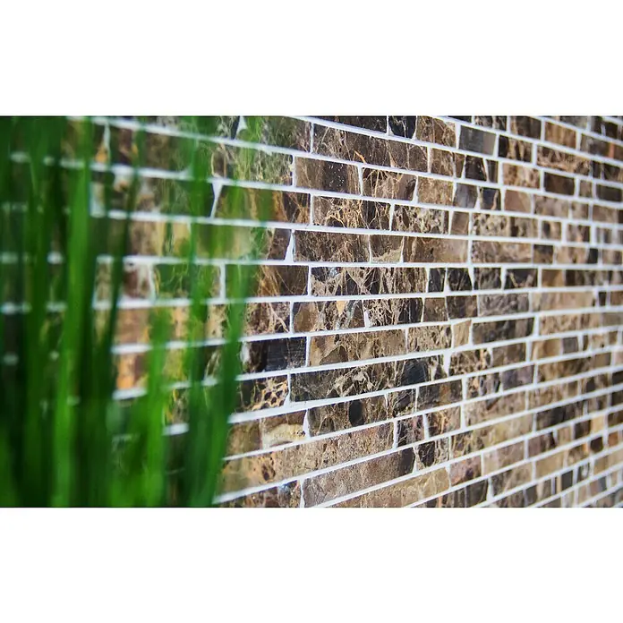 Mosaikfliese MOS BRICK 476 - 32,2 x 30,5 cm, Braun, Matt - Nahaufnahme einer Wand mit rechteckigen, braun marmorierten Fliesen und weißen Fugen, teilweise von grünem Gras verdeckt.