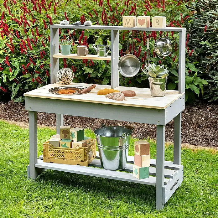 Muddy Buddy Matschküche Mud Starter - 80 x 40 x 90 cm, Holz, Natur/Wolkengrau - Ein grauer Muddy Buddy Spielküchentisch mit Spielzeugküchenutensilien im Garten. Perfekt für fantasievolles Spielen im Freien.