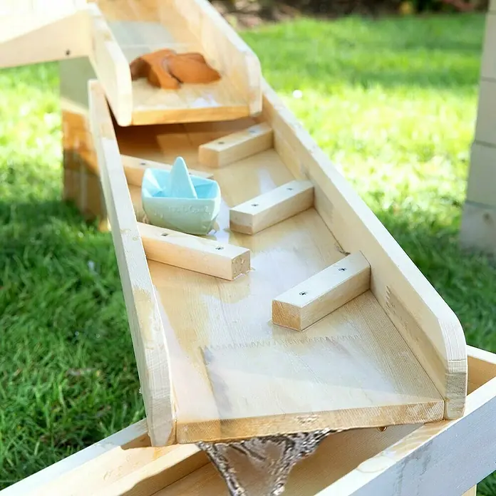 Muddy Buddy Wasserbahn Aqua Traveller - Holz, Natur/Wolkengrau - Nahaufnahme einer hölzernen Wasserrutsche mit kleinen Holzstegen, einem Spielzeugboot und einem Holzstern, die für spassige Wasserspiele im Garten konzipiert ist.