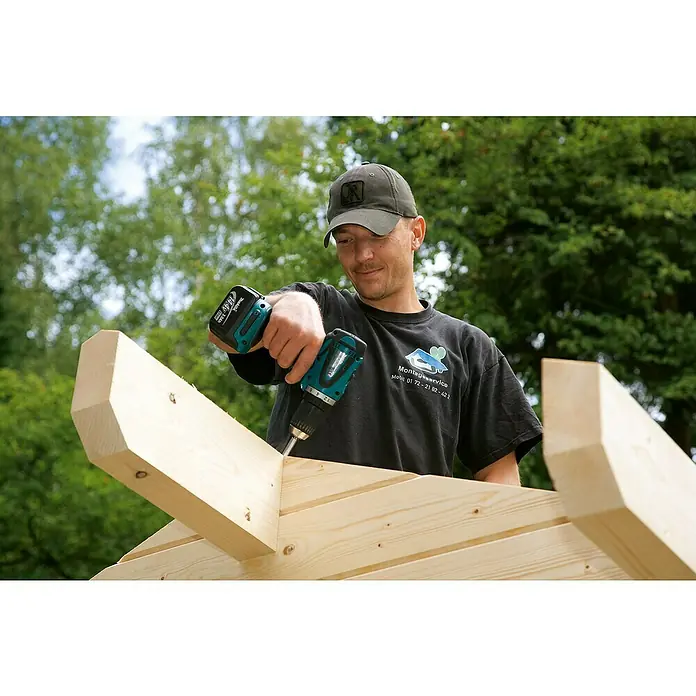 Skan Holz Gartenhaus Montreal 2Außenmaß inkl. Dachüberstand (B x T): 500 x 460 cm, Holz, Natur, 2 Lagen Dachschaltung - Ein Zimmermann befestigt Holzbalken mit einem Makita Akku-Bohrschrauber auf einer Baustelle. Der Bohrschrauber ist das Hauptaugenmerk.