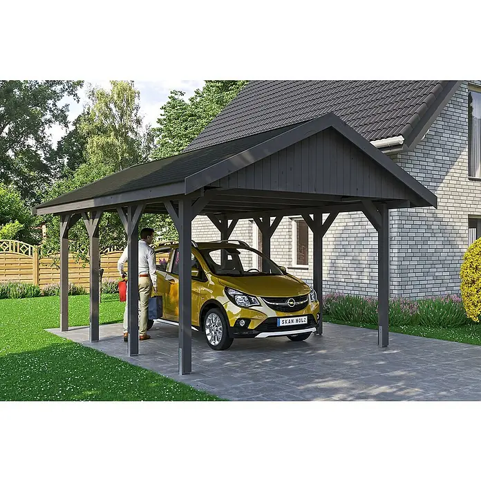 SKAN HOLZ Carport Wallgau - Außenmaß inkl. Dachüberstand (B x T): 4,3 x 6 m, Einzelcarport, Schiefergrau, Schwarze Bitumenschindeln - Ein gelbes Auto parkt unter einem stilvollen, dunklen Holzcarport neben einem Haus mit Ziegelmauerwerk. Die Konstruktion bietet optimalen Schutz vor Witterungseinflüssen.