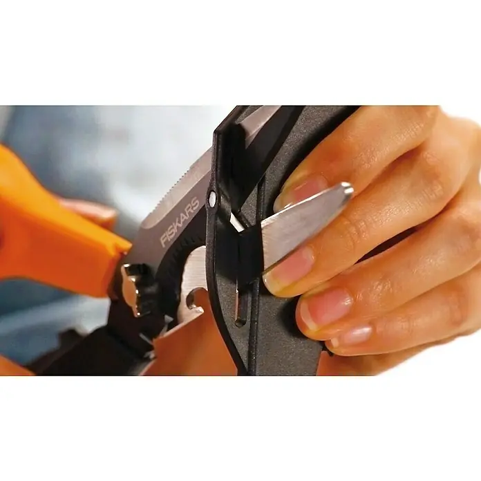 Fiskars Arbeitsschere Cut & More - Schnittlänge: 80 mm, Länge: 23 cm - Nahaufnahme einer Fiskars Mehrzweckschere beim Schneiden eines Gegenstandes, wobei die Schärfe und Vielseitigkeit des Werkzeugs hervorgehoben werden.