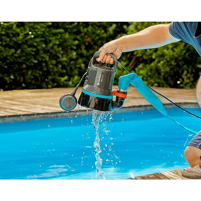 Gardena Bomba sumergible 9000 - 300 W, Capacidad de bombeo máx.: 9.000 l/h - Una bomba sumergible de agua clara Gardena 9000 Clear se sostiene sobre una piscina, con agua saliendo por la manguera de salida.