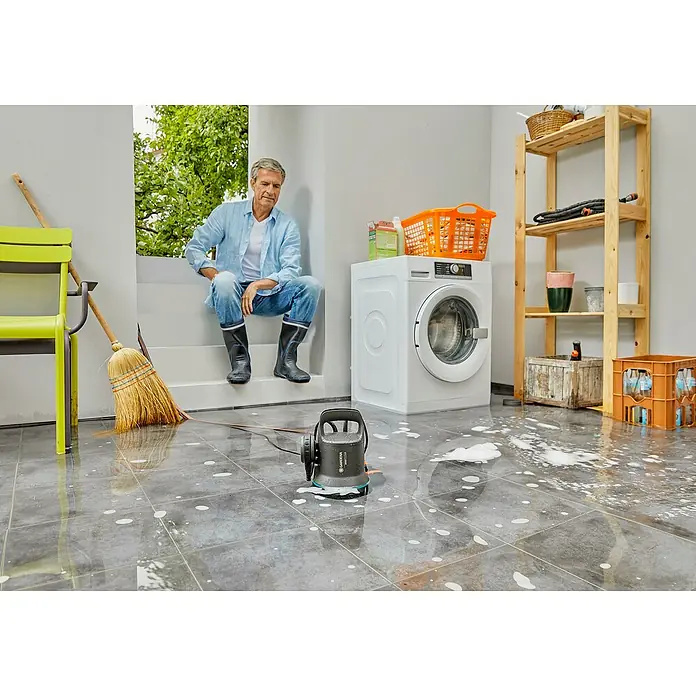 Gardena Bomba sumergible 9000 - 300 W, Capacidad de bombeo máx.: 9.000 l/h - Un hombre está sentado junto a una bomba sumergible para aguas sucias Gardena 7000, que se encuentra sobre un suelo de baldosas con agua y jabón.