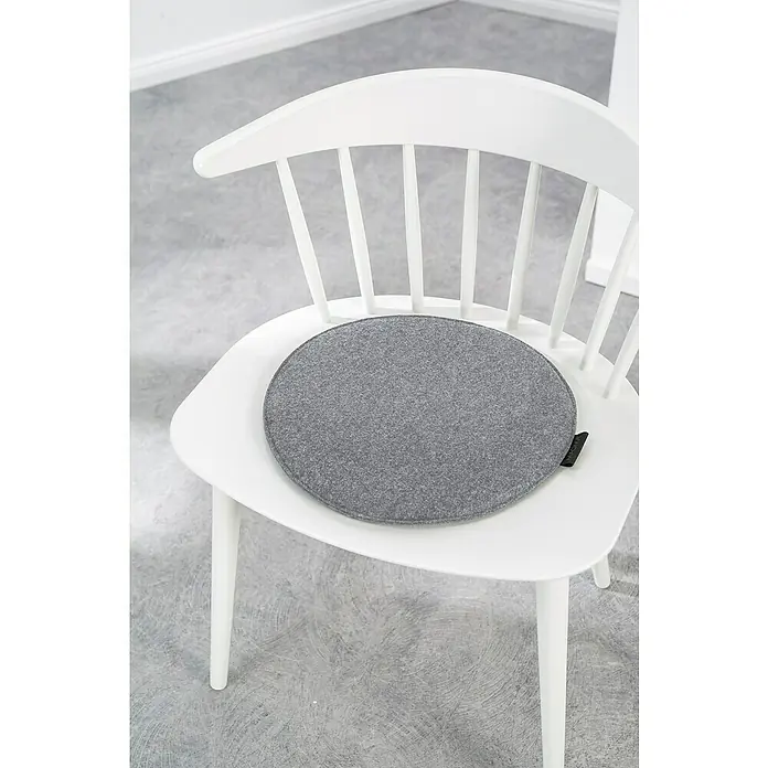 Sitzkissen rund Carl - Ø x H: 35 x 2 cm, Grau, 100 % Polyester - Eine Nahaufnahme eines weißen Holzstuhls mit einem runden, grauen Sitzkissen darauf. Das Kissen ist aus Filz mit einer kleinen schwarzen Schlaufe.