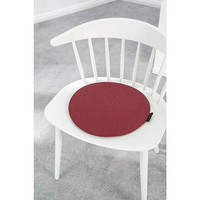 Sitzkissen rund Carl - Ø x H: 35 x 2 cm, Weinrot, 100 % Polyester - Das Bild zeigt ein rundes, weinrotes Sitzkissen auf einem weißen Holzstuhl, das für Komfort und Stil sorgt.