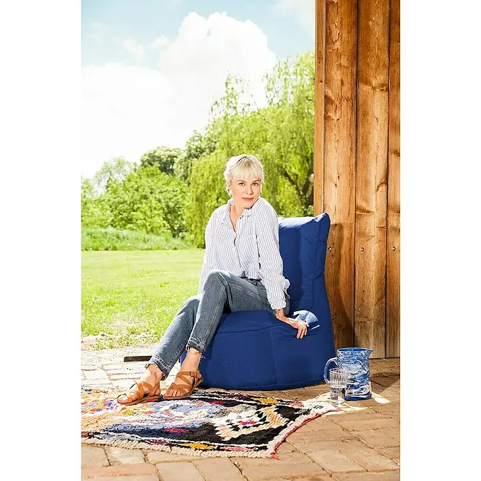 Sitzsack Swing Scuba Set inkl. Dotcom - 95 x 90 cm, Blau, 100 % Polyester/100 % Polyvinylchlorid - Eine Frau sitzt auf einem blauen Sitzsackstuhl im Freien, neben ihr ein Krug und ein Glas Wasser auf einem bunten Teppich.