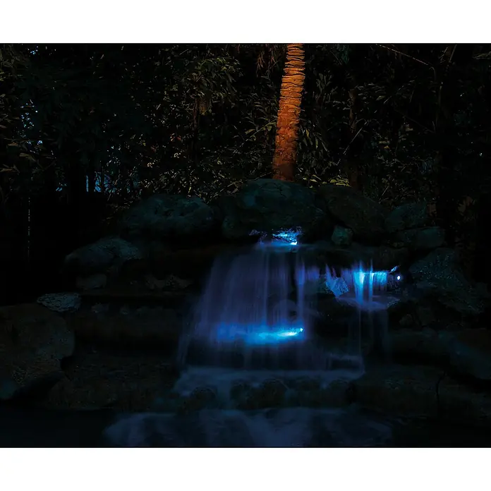 Pontec Teichbeleuchtung PondoStar LED - 3 Stk., Lichtfarbe: RGB - Nächtlicher Wasserfall mit blauer Beleuchtung, umgeben von tropischer Vegetation und einem Palmenstamm.