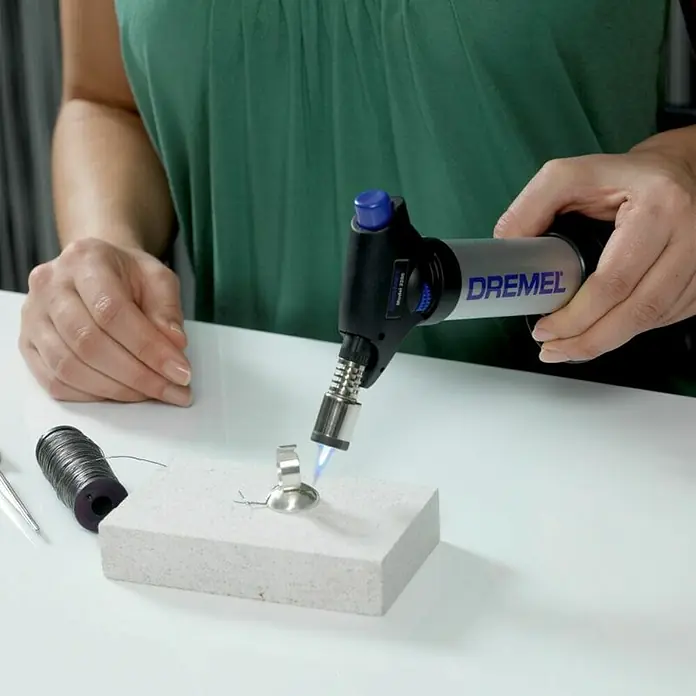 Dremel VersaFlame Unidad de soldadura de alto rendimiento 2200-4 - Apto para: Gas butano - Una mujer usa un soplete Dremel para trabajar en una joya sobre un ladrillo refractario.\n