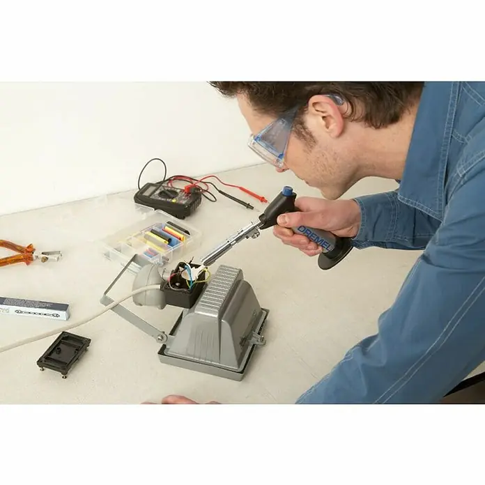 Dremel VersaFlame Unidad de soldadura de alto rendimiento 2200-4 - Apto para: Gas butano - Un hombre utilizando un soplete de soldadura Dremel para trabajar en un artefacto de iluminación eléctrica mientras usa gafas de seguridad.