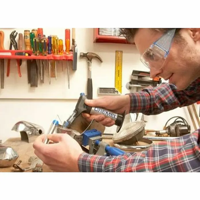 Dremel VersaFlame Unidad de soldadura de alto rendimiento 2200-4 - Apto para: Gas butano - Primer plano de un hombre usando un soplete de soldadura Dremel sobre metal, con gafas de seguridad, ideal para trabajos de precisión.
