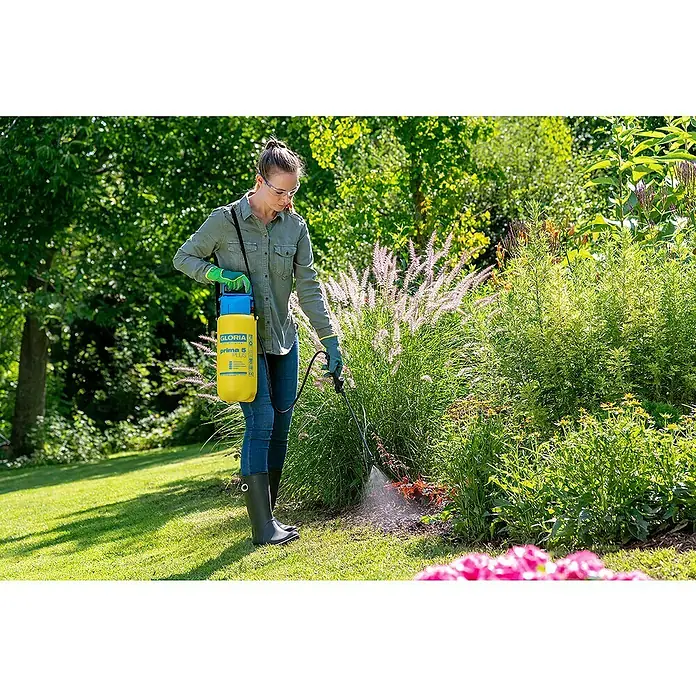 Gloria Drucksprühgerät Prima 5 PLUS - 5 l - Frau sprüht mit einer gelben Gloria Prima 5 Plus Druckspritze Unkraut im Garten, geschützt mit Brille und Handschuhen.
