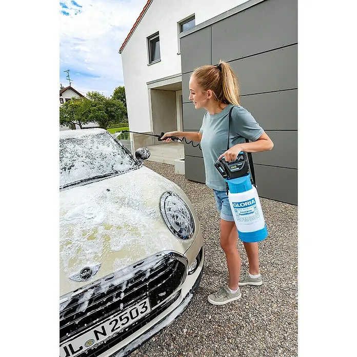 Gloria Akku-Kompressor - 18 V, Ohne Akku - Eine Frau wäscht ein Auto mit einem Gloria FoamMaster FM30 Akku-Schaumsprüher, der über der Schulter hängt und Schaum versprüht.