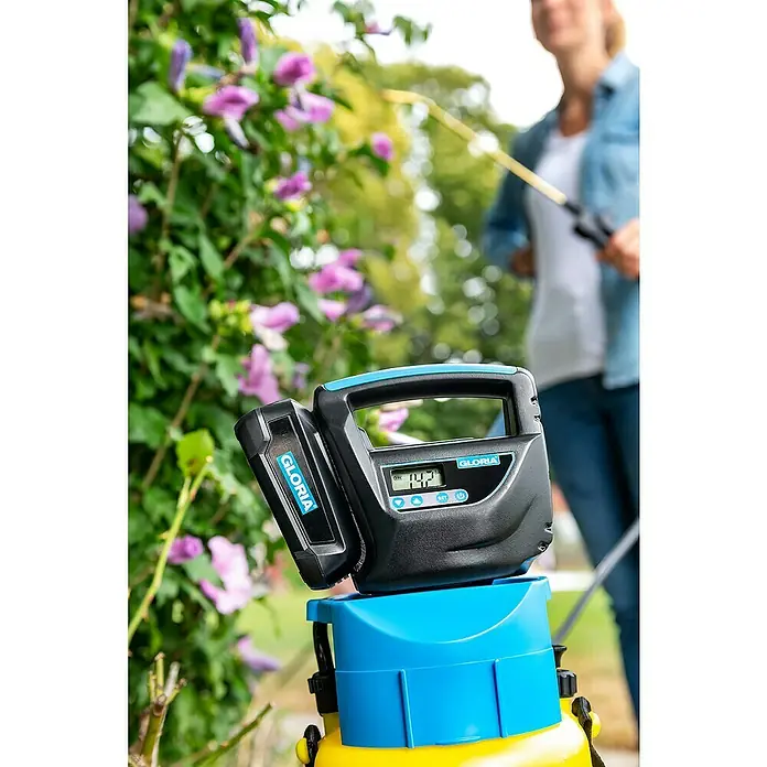 Gloria Akku-Kompressor - 18 V, Ohne Akku - Nahaufnahme eines GLORIA Drucksprühers mit digitaler Steuerung vor blühenden Pflanzen, bedient von einer Frau.