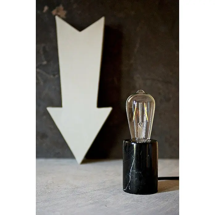 Home Sweet Home Lampenfuß Dry - 10 W, E27, Schwarz, Höhe: 10 cm - Elegante Tischleuchte mit Edison-Glühbirne auf einem Sockel aus schwarzem Marmor, daneben ein weißer Pfeil vor dunklem Hintergrund.