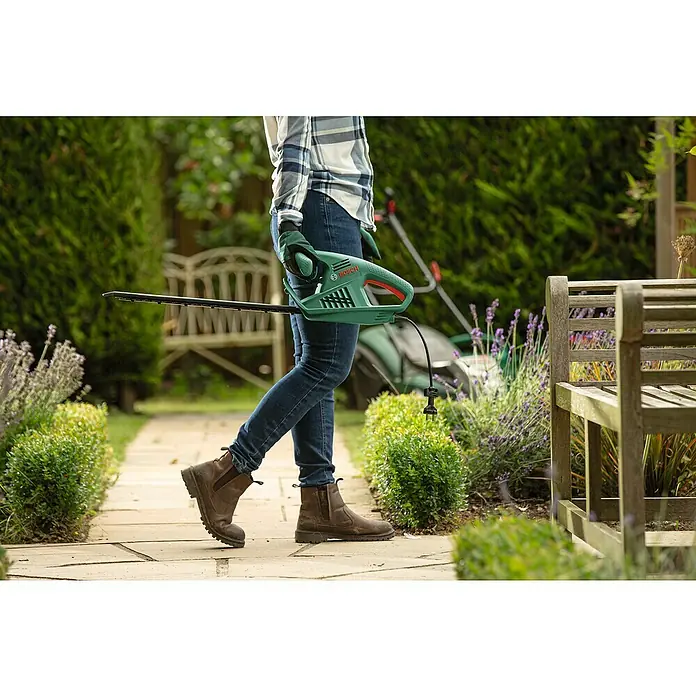 Bosch Elektro-Heckenschere EasyHedgeCut 55 - 450 W, Schnittlänge: 55 cm - Eine Person hält eine grüne Bosch Heckenschere in einem Garten.