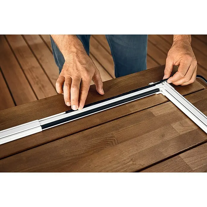 Tesa Insect Stop Puerta con protección contra insectos Falt - Blanco, Montaje de la mosquitera: Pinzas - Primer plano de una mosquitera con una persona que adjunta la fijación a una mesa.