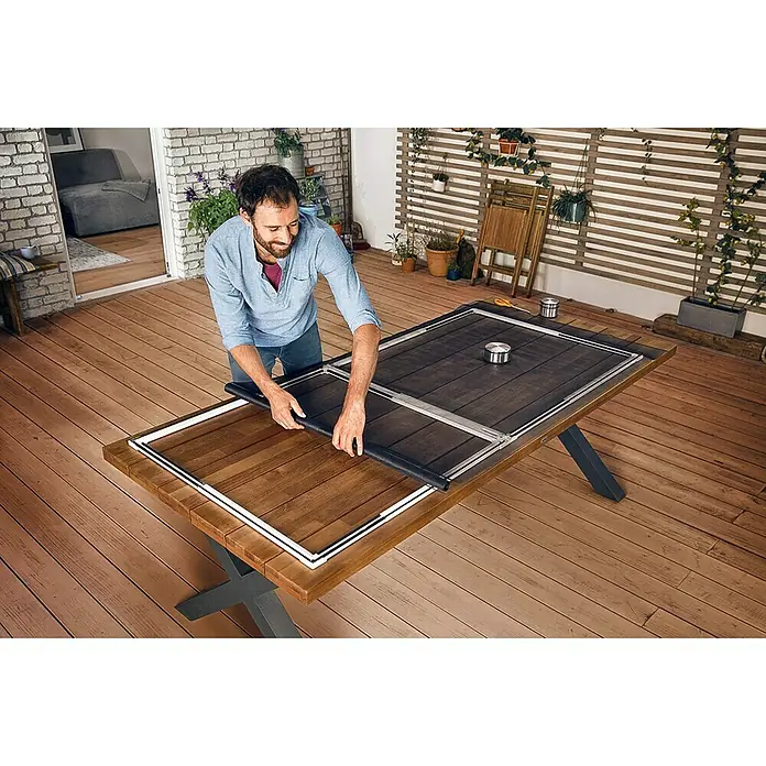 Tesa Insect Stop Puerta con protección contra insectos Falt - Blanco, Montaje de la mosquitera: Pinzas - Un hombre monta un marco de pantalla sobre una mesa de madera al aire libre. El producto es un marco de pantalla.