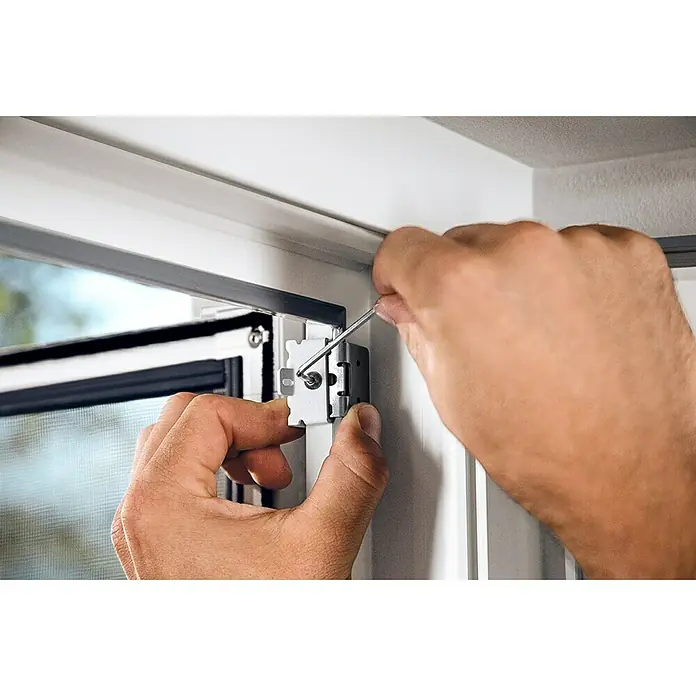 Tesa Insect Stop Puerta con protección contra insectos Falt - Blanco, Montaje de la mosquitera: Pinzas - Un primer plano de alguien que usa un destornillador para asegurar un soporte de ventana plateado en un marco de ventana blanco.