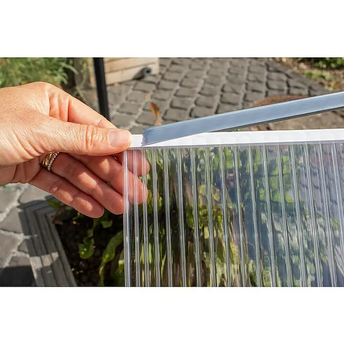 Pergart Gewächshaus-Abdichtung HKP M - Passend für: Pergart Gewächshäuser 5000-6500, 3 Stk. - Nahaufnahme einer Hand, die eine transparente, mehrwandige Polycarbonatplatte mit einem grauen Profil hält.