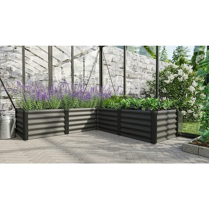 Vitavia Hochbeet Meta In&Out 401 - 185 x 185 x 40 cm, Zincalume®, Granit/Schwarz - Das Bild zeigt erhöhte Gartenbeete aus Stahl mit Lavendel und Kräutern vor einer Steinmauer und einem Gewächshaus.