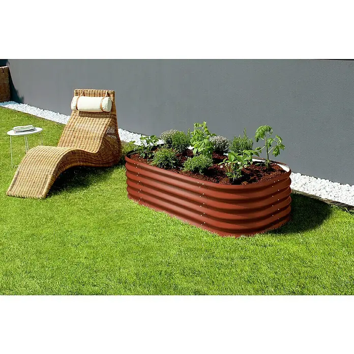 Vitavia Hochbeet Terra 401 - 162 x 82 x 40,1 cm, Zincalume®, Rubin - Ein braunes Hochbeet aus Metall mit Pflanzen steht auf einem grünen Rasen, daneben ein Rattansessel. Ideale Gartenausstattung für Hobbygärtner.