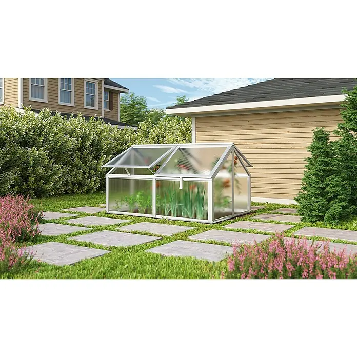 Vitavia Frühbeet Zola - 124,3 x 89 x 71,3 cm, Silber, Polycarbonat - Ein kleines Gewächshaus aus Metall und Kunststoff im Garten, umgeben von Pflanzen und Steinen.