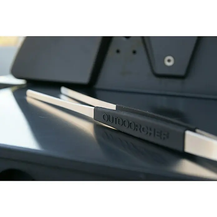 Outdoorchef Grillbesteck - Länge: 45 cm - Grillzange von Outdoorchef. Die Zange ist aus Edelstahl mit einem schwarzen Griff und liegt auf einem Grill.