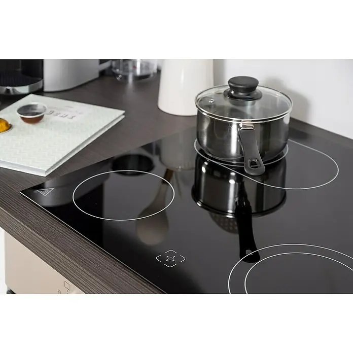 Respekta Premium Winkelküche RP260EWCBO - B x T: 260 x 60 cm, Weiß, Mit Elektrogeräten - Ein Kochtopf mit Deckel steht auf einem modernen schwarzen Glaskeramikkochfeld in einer Küche, daneben ein Buch und Küchenutensilien.