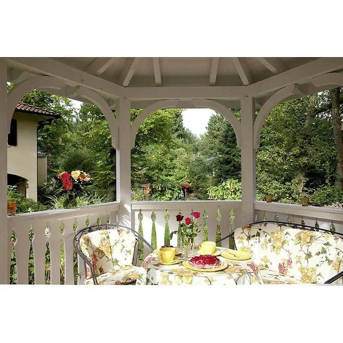 SKAN HOLZ Pavillon Nancy 3 - L x B: 416 x 480 cm, Weiß - Ein gemütlicher Tisch mit floralem Tischtuch, Geschirr und Kuchen in einem weißen Gartenpavillon, umgeben von üppigem Grün.