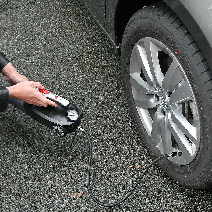 Aspirador de mano de batería Autovac - 50 W, Volumen de recipiente: 0,15 l - Inflador de neumáticos en acción. Una persona infla un neumático con un inflador portátil negro equipado con un manómetro.