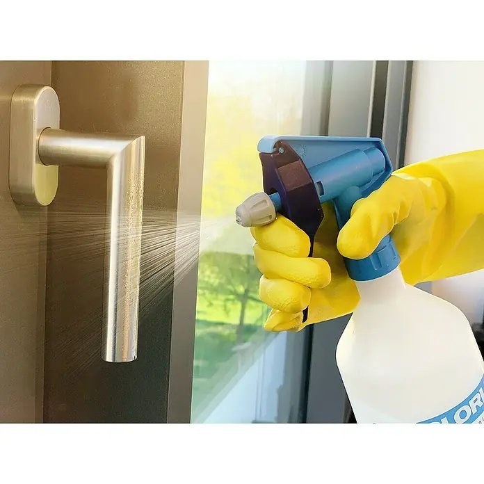 Gloria Feinsprüher Clean Master EXTREME EX 10 - Füllmenge: 1 l, Geeignet für: Desinfektionsmittel - Eine Hand mit gelbem Handschuh sprüht Desinfektionsmittel auf einen Türgriff, um ihn sauber zu halten und die Ausbreitung von Keimen zu verhindern.