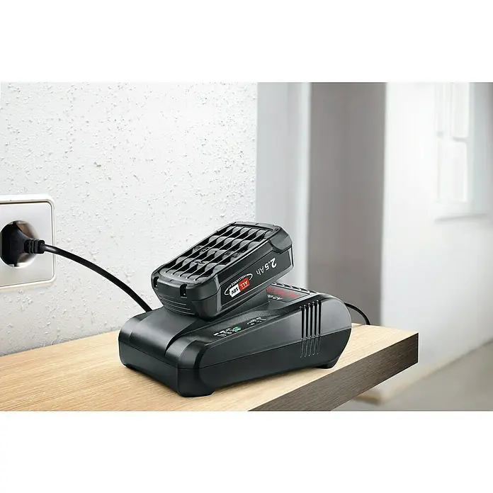 Bosch Power for All 18V Ladegerät AL 1880 CV - Passend für: Bosch Heimwerker- & Gartengeräte-Akkus 14,4/18 V - Akkuladegerät mit einem Bosch-Akku der 18V Power for All Alliance, 2.5 Ah, mit Netzstecker in der Steckdose auf einer Holzoberfläche.