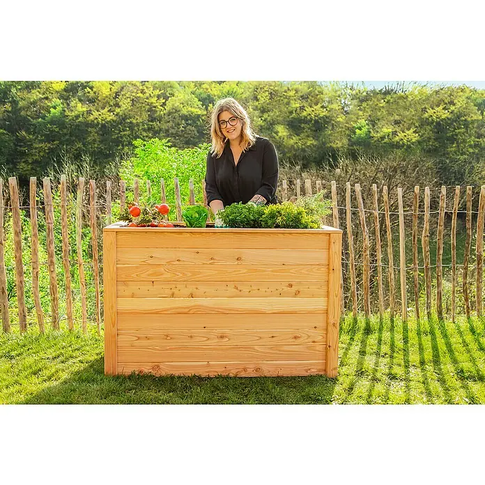 Westmann Hochbeet Lärche 130 - 130 x 65 x 84 cm, Holz, Natur - Holzhochbeet mit verschiedenen Gemüsesorten und einer Frau im Hintergrund. Perfekt für den Garten oder die Terrasse.
