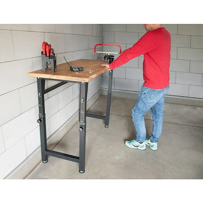 Rikta Werkbank Höhenverstellbar - L x B: 60 x 135 cm, Arbeitshöhe: 105 cm, Belastbarkeit: 200 kg - Ein höhenverstellbarer Werktisch mit Werkzeugen und einer Person, die daran arbeitet. Der Tisch hat eine robuste Konstruktion.