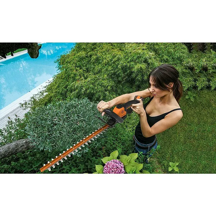 Worx PowerShare 20V Akku-Heckenschere WG261E.9 - 20 V, Li-Ionen, Ohne Akku, Schnittlänge: 45 cm - Eine Frau bedient eine Akku-Heckenschere von Einhell im Garten, umgeben von üppigem Grün und einem Pool im Hintergrund.