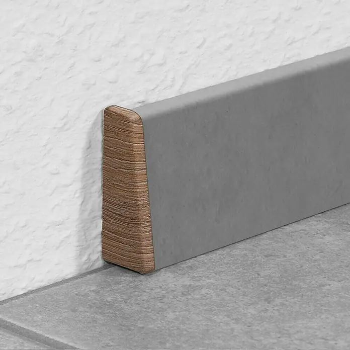LOGOCLIC Endkappe K40 C - Kastanie, 2 Stk., Passend für: LOGOCLIC Sockelleiste K40 C - Ein grauer Fliesenfußleiste mit einer holzähnlichen Endkappe vor einer weißen Wand und einem grauen Fliesenboden.