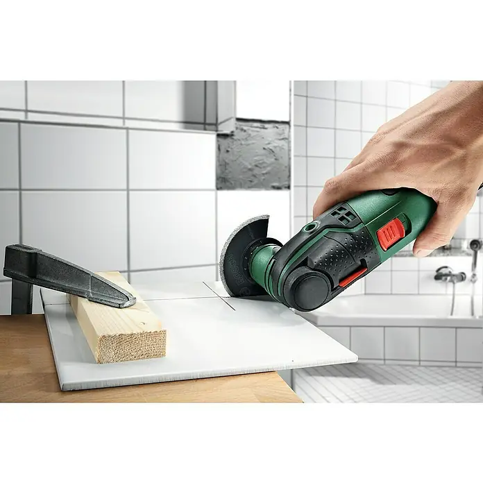 Bosch Power for All 18V Multiherramienta de batería Advanced Multi 18 - 18 V, Sin batería - Una multiherramienta verde de Bosch cortando una baldosa asegurada con una abrazadera, sobre un fondo de baño.