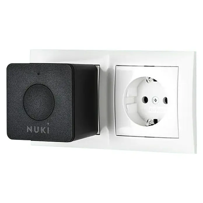 Nuki Módulo transmisor inalámbrico Bridge - Específico para: Cerradura electrónica Nuki, Negro - Primer plano de un enchufe Nuki Smart Lock junto a una toma de corriente.