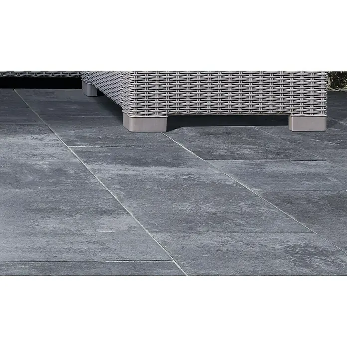EHL Terrassenplatte BAUHAUS - 50 x 25 x 4 cm, Nero, Beton - Nahaufnahme von grauen Terrassenfliesen, die einen modernen Außenbereich mit einem stilvollen Rattanmöbelstück schaffen. Die Fliesen sind robust und pflegeleicht.